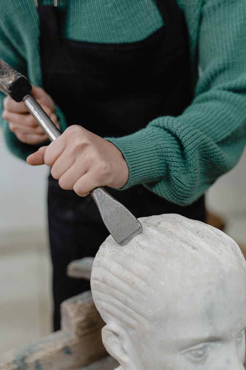 A sculptor skillfully uses a chisel to shape a marble statue indoors, showcasing artistry and craftsmanship.
